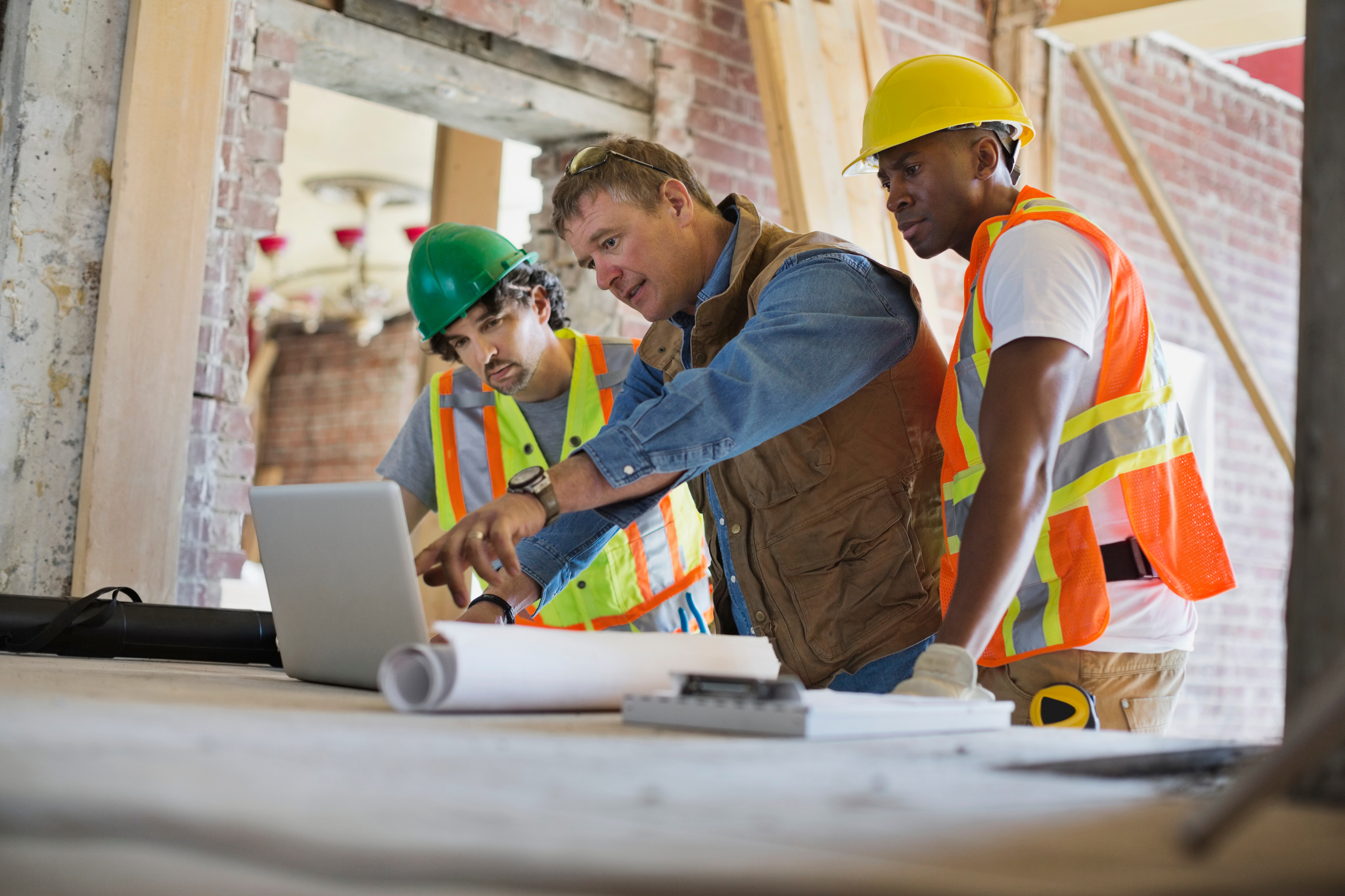 Foreman discussing plan on laptop with tradesmen at construction site